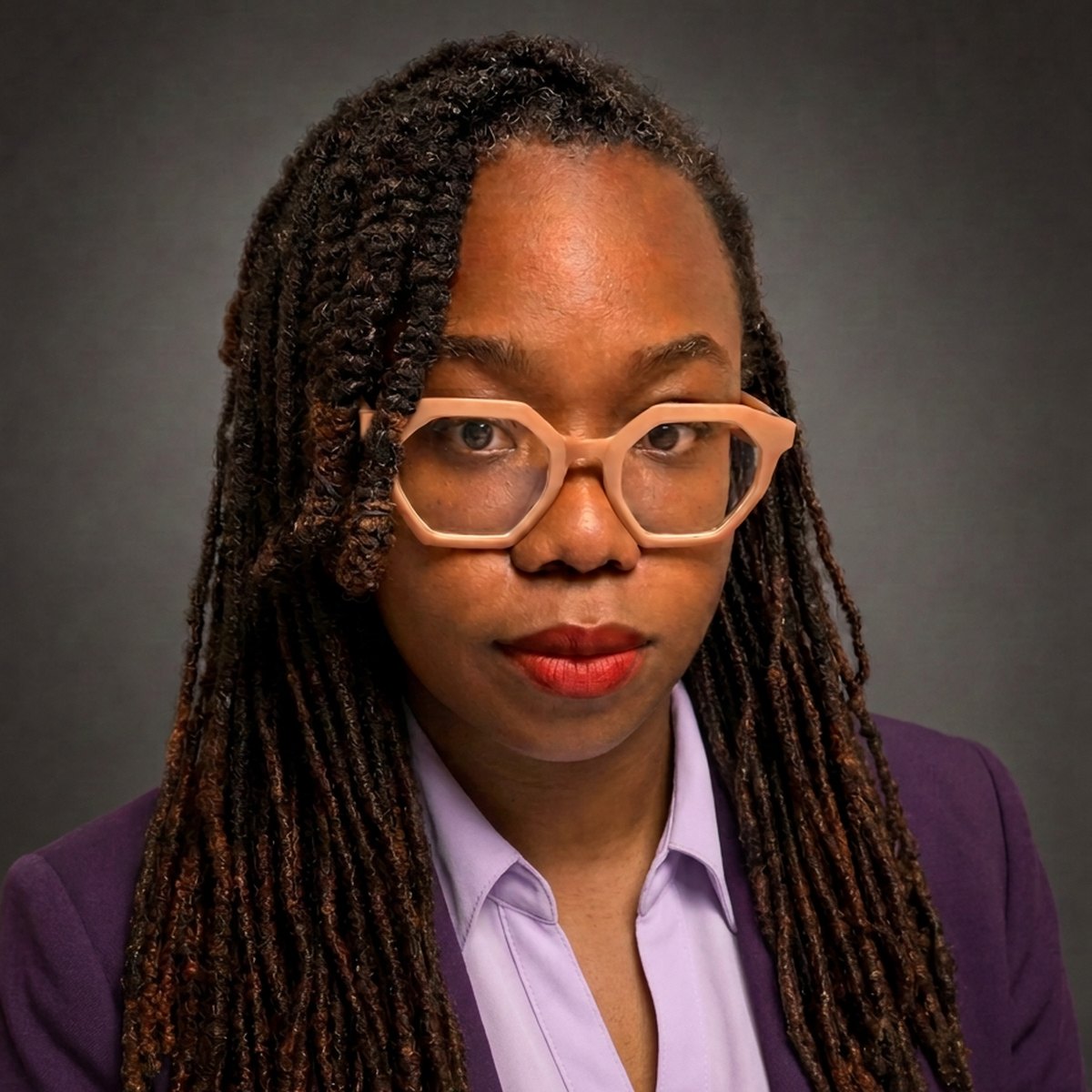 Professional headshot of Nana Nwachukwu in a purple blazer and lavender blouse against a dark background