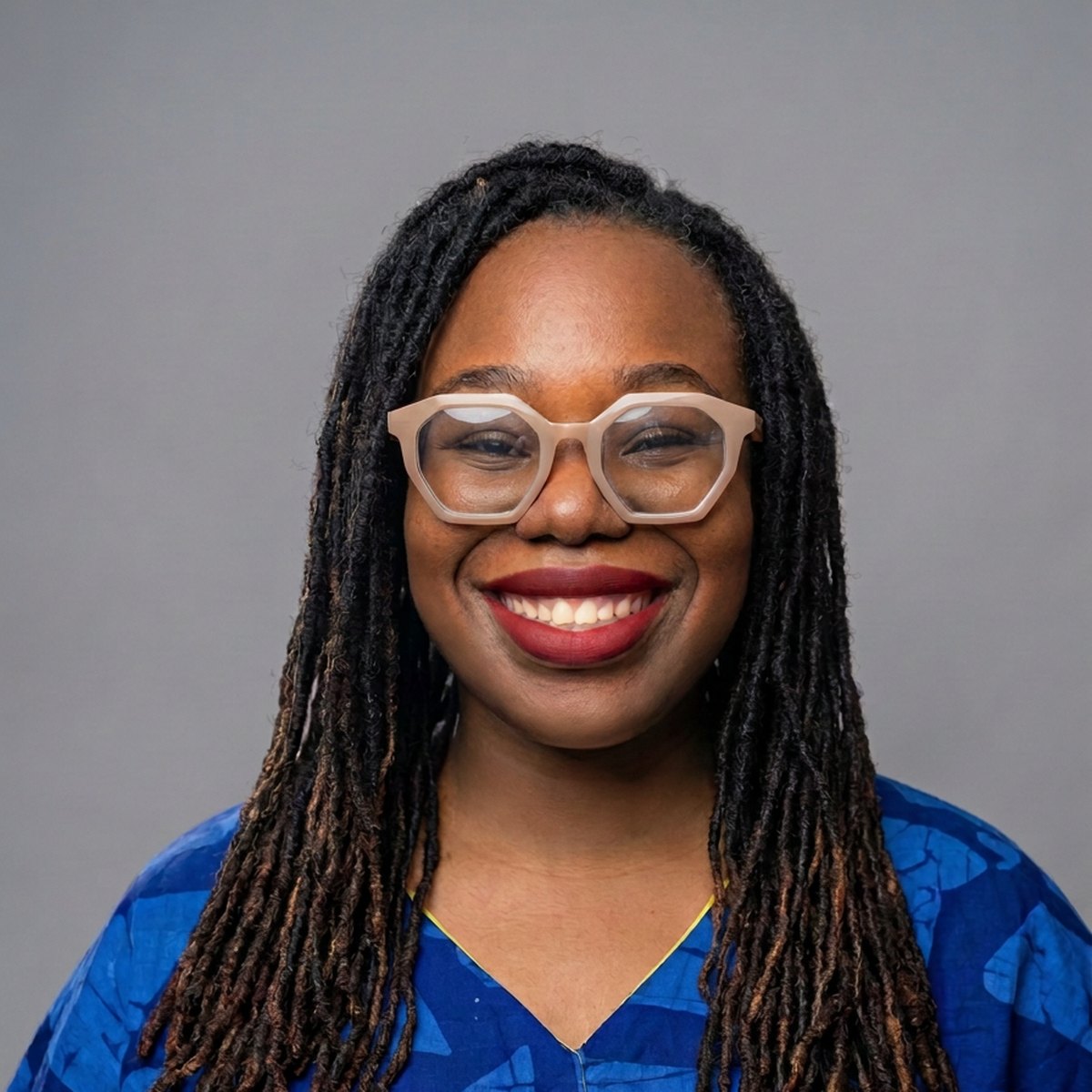 Nana Nwachukwu smiling warmly, wearing light-framed glasses and a blue patterned top