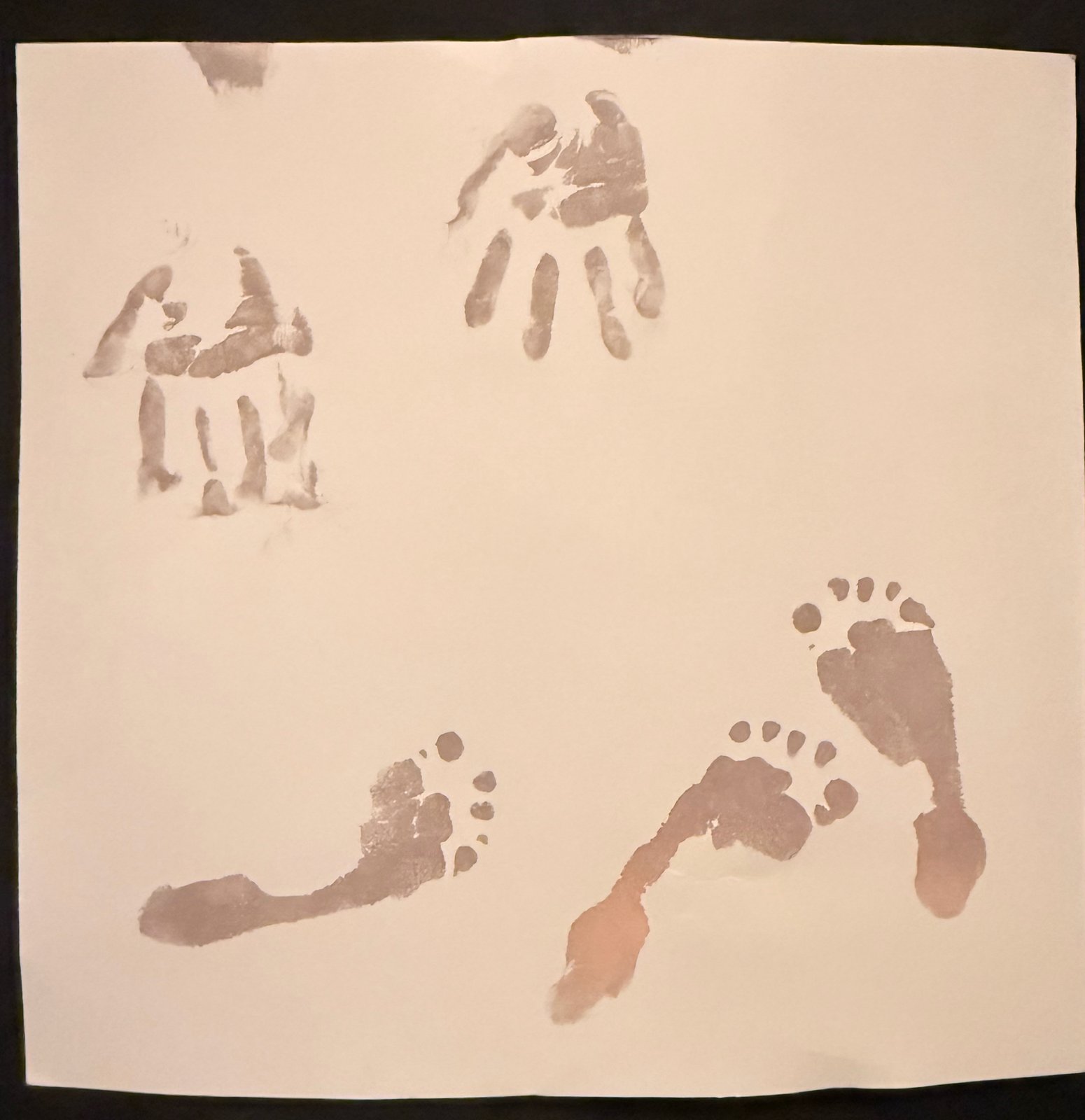 Two small brown handprints and two small footprints stamped on a sheet of white paper.