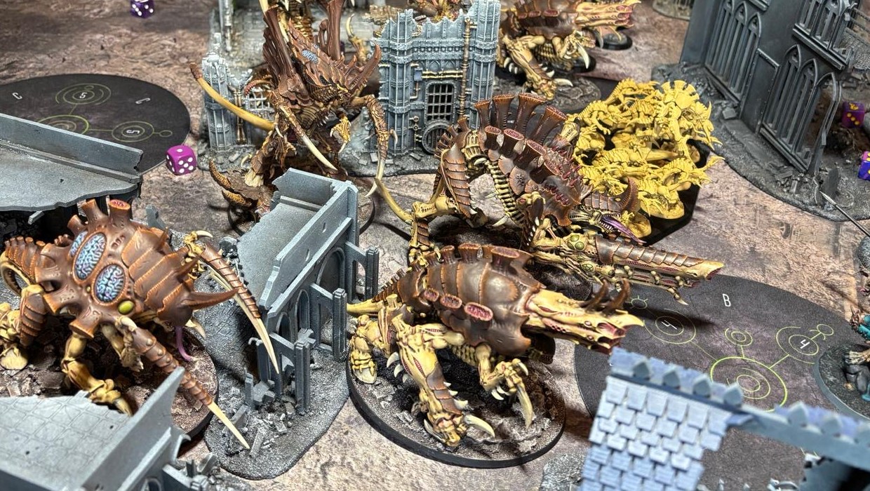 A painted bug-alien army battling among gothic ruins on a tabletop gaming mat.