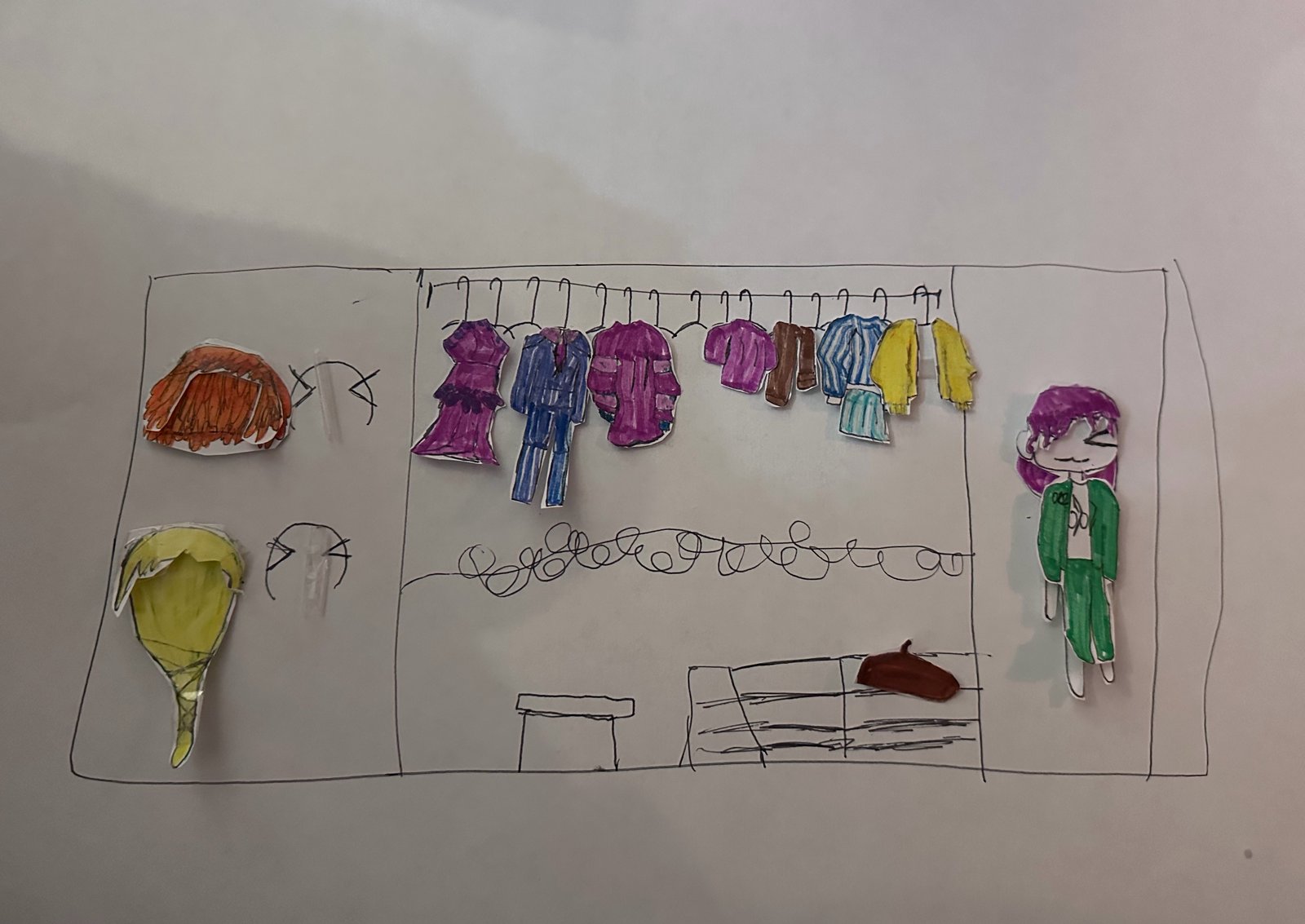 A paper dress-up wardrobe drawn in pen, with cut-out coloured clothes on a rail, hats on a shelf, a shoe, and a paper doll lying at the bottom.