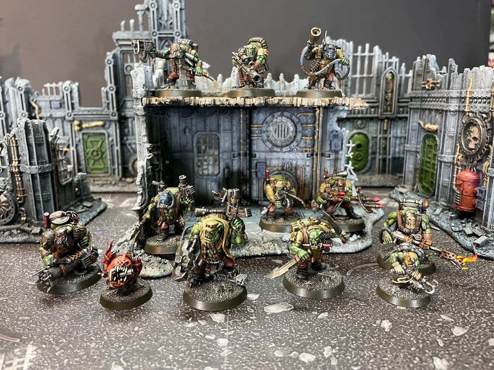 An orc squad of painted miniatures lined up in front of painted industrial ruins.